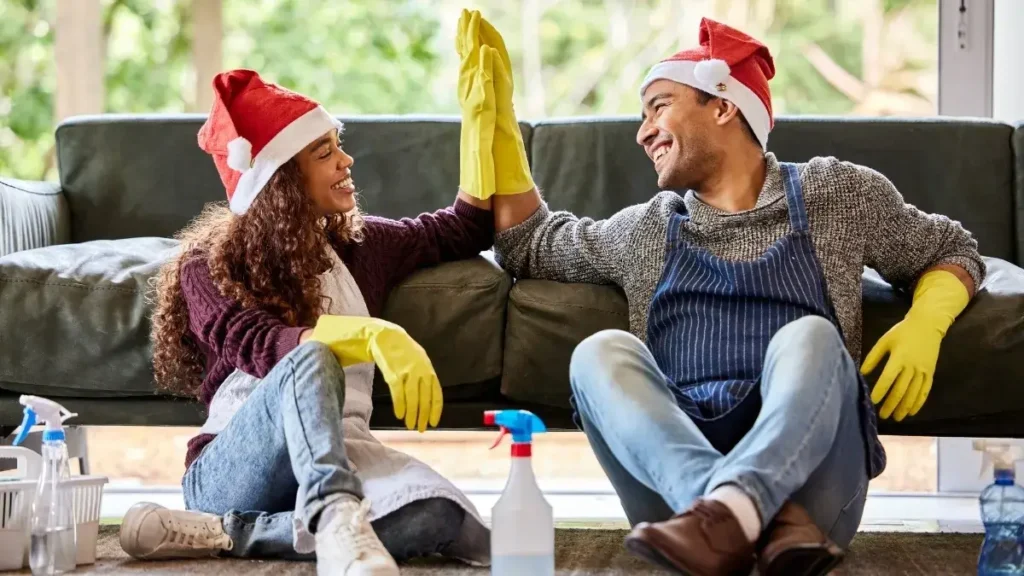 Couple wearing Christmas hats cleaning the living room and high fiving during a holiday cleaning checklist