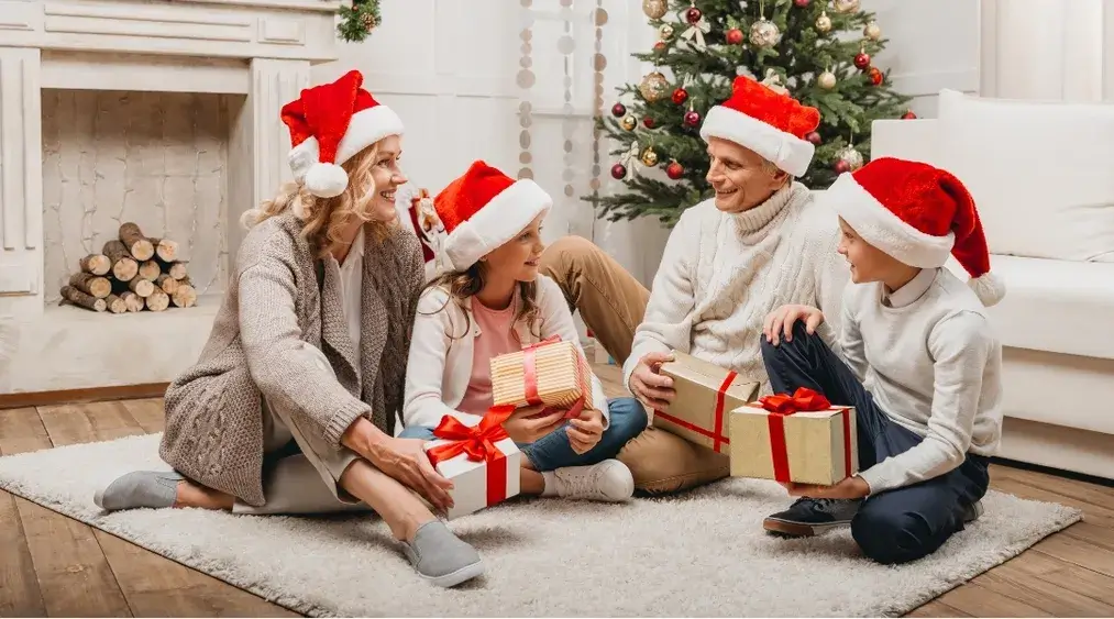 Family celebrating Christmas together at home wearing Santa hats and exchanging gifts