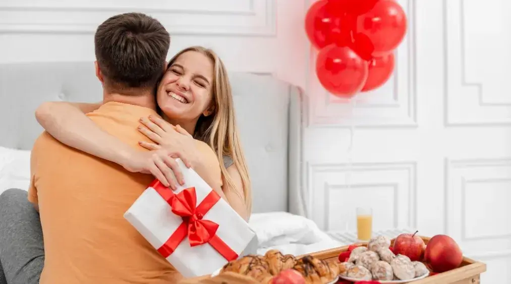 Couple celebrating Valentine’s Day in a clean, cozy bedroom with balloons and gift
